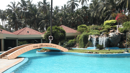 A view of the pool at The Retreat Hotel and Convention Centre with a bridge, canopies and trees in view