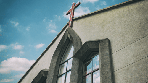 A church building with a cross on the roof against a blue sky with clouds.