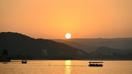 A picturesque view of lake pichola with a boat in the waters and sun setting in the background