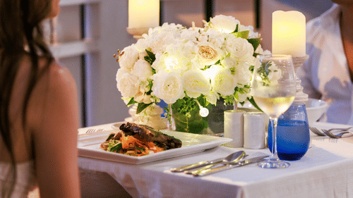 A table set with white flowers, candles, plated food, and wine at The Soco House, with two diners partially visible.