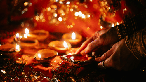 A pair of hands lighting up traditional Indian lamps as some of them are already lit