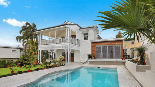 a large swimming pool next to a big townhouse with blue sky in the background