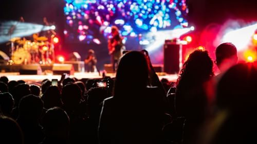 Audience silhouettes watch a brightly lit concert stage from a distance.