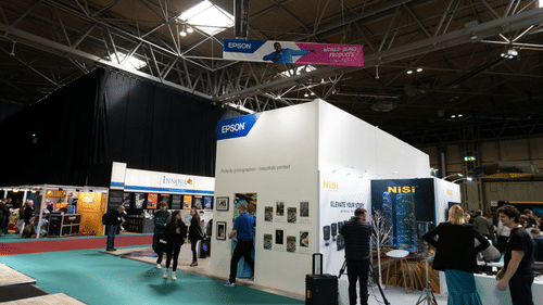 An overview of an exhibition centre with a stall in the centre and people walking around.