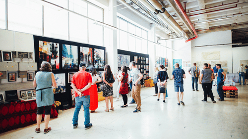 An overview of a exhibition with stalls on one side and people walking next to it.
