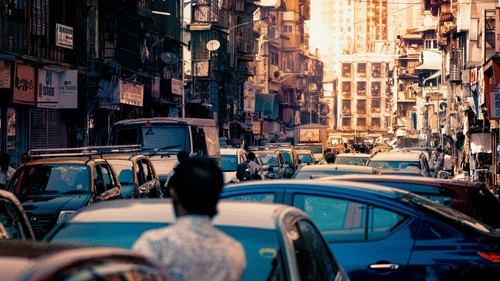 Busy urban street in Mumbai with cars and tall buildings at sunset.