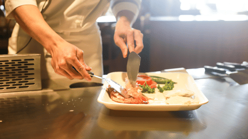 A close up of a chef wearing a uniform preparing a plate of food in the kitchen.