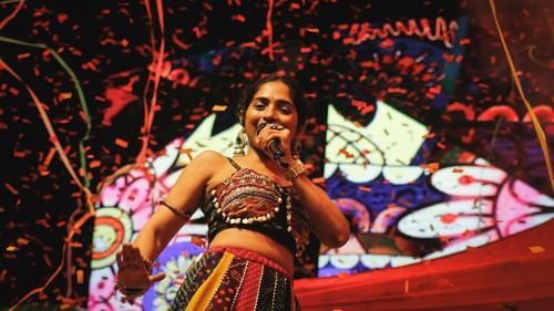A female singer performs on stage with colourful lights and a vibrant backdrop behind her.