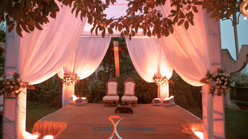 A wedding stage with draped fabric and floral decorations is set up outdoors at Tijara Fort-Palace - 19th Century, Alwar, beneath tree branches.