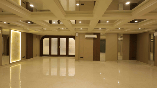 A large, empty banquet hall at Tulip Inn Gurugram with polished white floors, wood-panelled walls, and a multi-level recessed ceiling with warm lighting.