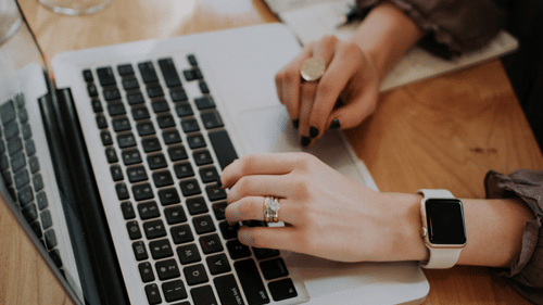 A person's hand browsing on the laptop on a wooden table