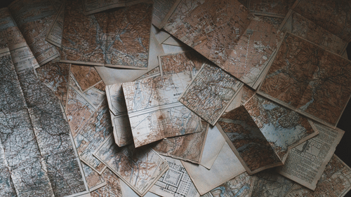 A collection of old, unfolded maps spread out, covering the entire surface beneath them.