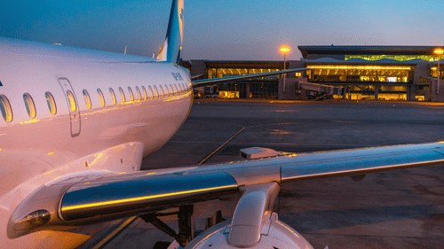 A passenger airplane parked at an airport runway during evening with terminal lights in the background.