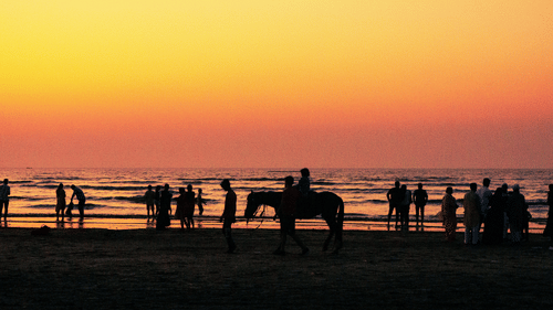 Visitors enjoying an evening at Daman Beach as the sun sets over the Arabian Sea, with silhouettes of people and a horse ride along the shoreline