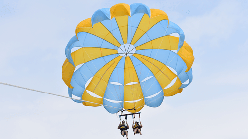 A view from below of a couple strapped to a parachute while performing a parasailing activity.