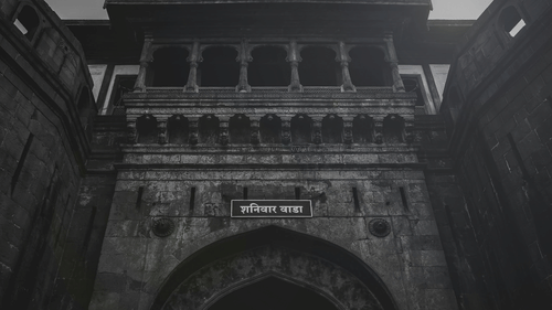A stone gateway with an arched entrance, balconies with railings above, and a signboard mounted over the arch against the sky.