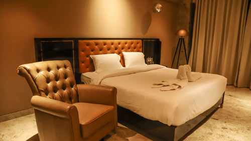 A king bed with a plush headboard and a single seater sofa next to the bed inside one of the rooms at VITS Nanded Hotel.