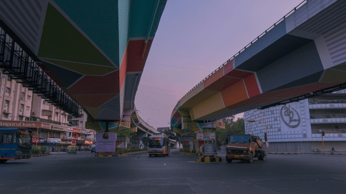 Low-angle view of 2 flyovers with underpasses painted in vibrant geometric colours at dusk.