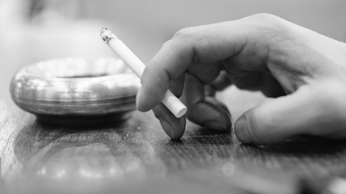 A person holding a cigarette next to an ash tray