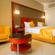 Hotel room at Featherlite Evoma Hotel with a bed dressed in yellow and white linen, a yellow armchair and a round red side table nearby.