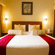 Hotel room at Featherlite Evoma Hotel with a bed dressed in white and maroon linen, a wooden headboard and framed wall art placed nearby.