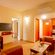 Suite living area at Featherlite Evoma Hotel with a red sofa, a wall-mounted television, a kitchenette and warm wooden flooring below.