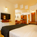 Hotel room at Featherlite Evoma Hotel with a bed dressed in white and dark grey linen, a wall-mounted television and a seating area nearby.