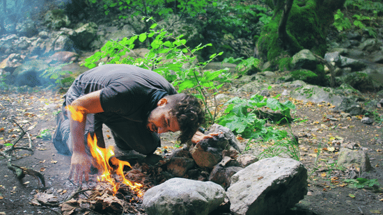 A person is cooking over a fire outdoors using stones.