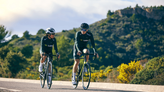 A view of 2 people cycling on road with scenic hill on the backdrop 