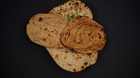 An assortment of plain and stuffed parathas arranged on a dark surface.