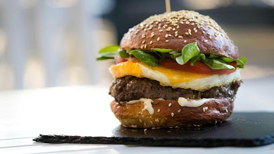 A juicy burger with cheese, lettuce, and a fried egg on a dark bun.