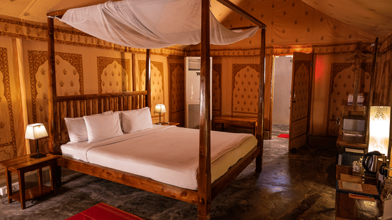 A room with a wooden 4-poster bed with 2 bedside lamps against patterned walls and a small work desk opposite to it at Barefoot at Havelock.