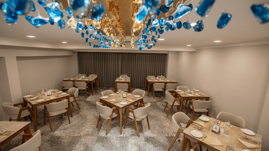 Elegant dining room at Biznotel by Pride Surat featuring vibrant blue glass chandeliers and wooden tables.