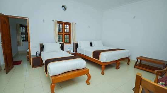 A king bed with a single bed next to it in Deluxe Quadruple room - Capitol Village Resort, Madikeri