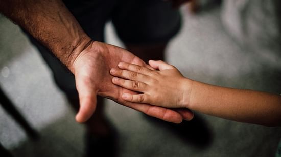 A child placing their hand over an adult's hand, symbolising love, trust, and the bond between a father and child.