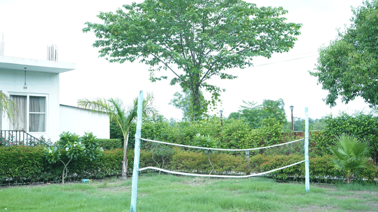 Lawn volleyball net supported by white poles set up on a lush green grass field surrounded by trees and resort greenery - Five Elements Hotels, Corbett Crown Resort, Jim Corbett
