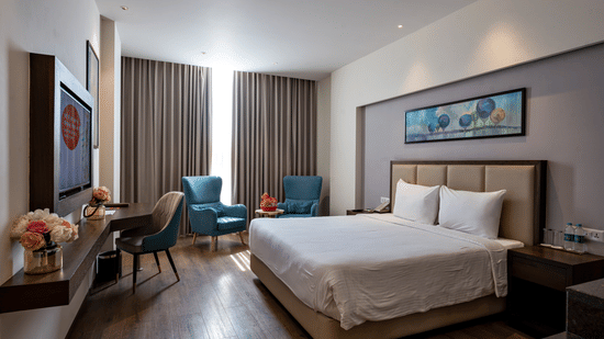 A bedroom at Geeta Sarovar Portico, Panipat featuring a double size bed, a flat TV screen on the wall, a chair, and a seating area.