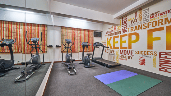 A fitness centre with elliptical machines, a treadmill, exercise mats, and a wall with typography | HHI Varanasi