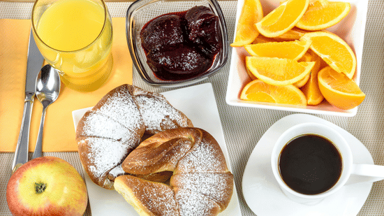 Breakfast spread with croissants, jam, orange slices, coffee, and juice.