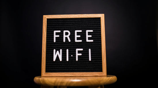 A black felt letter board with the words 'FREE WI-FI' in white letters, sitting on a wooden stool.