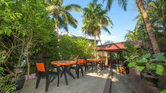 Outdoor seating with coconut trees among other trees at Love Garden in Hotel Shompen, one of the best hotels in Port Blair.