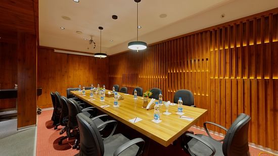 A modern and well-equipped meeting room at Icon Boutique Hotel by Bhagini, Domlur, with a long conference table, chairs, and a wooden wall.