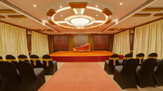 Rows of black chairs, a central red carpet, and a small stage in the event hall at Icon Express By Bhagini, Mahadevapura.