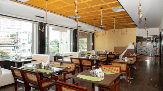 Seating area in the dining hall featuring large windows, multiple tables, and wooden chairs, at Icon Express By Bhagini, Mahadevapura.
