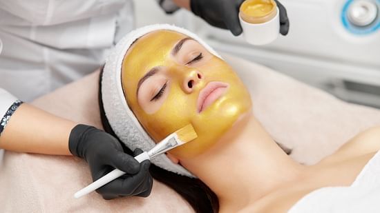 A woman getting a gold facial mask applied to her face