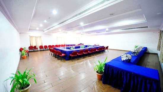 A spacious Pearl hall featuring a U-shaped table arrangement, buffet setup to the right, wooden floor, potted plants, and with windows and curtains