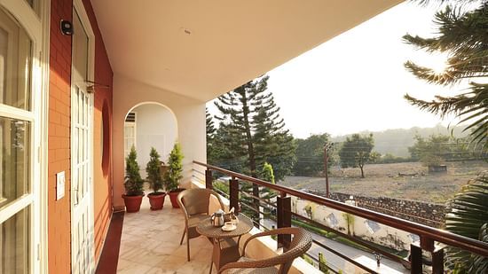 An image of a balcony where chairs are placed from where green trees and plants can be seen - Lamrin Boutique Cottages Rishikesh