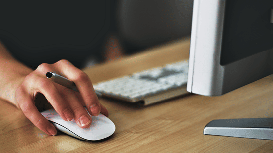 Close-up of a hand using a computer mouse at a wooden desk.