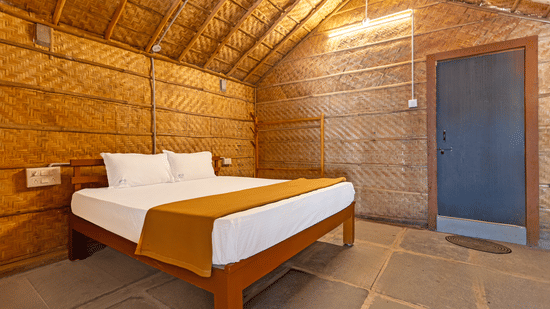Rustic cottage interior with a high thatched roof, woven walls, and a large wooden bed - Nature Trails Ashoka Resort Hampi