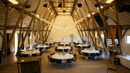 Interior of a large reception hall with high-pitched wooden-beam ceilings and formal dining setups.